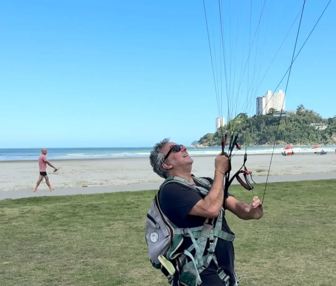 Aluno controlando a vela no gramado da Praia do Itararé, com o morro ao fundo