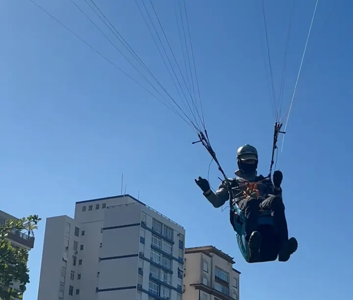 Piloto voando de parapente acima dos prédios da orla