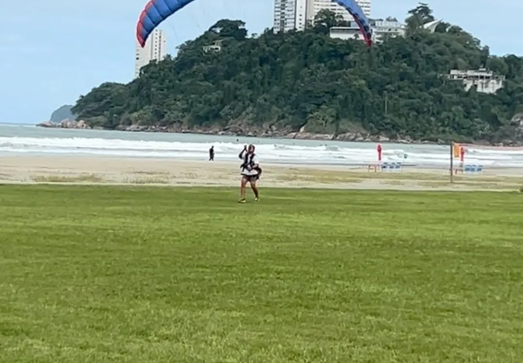 Parapente aberto acima do gramado da praia, com o Morro do Itararé ao fundo